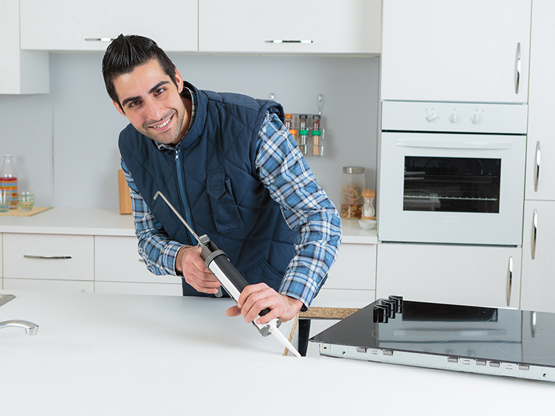 Küchenmonteur montiert präzise Küchenschränke und Geräte bei einer Küchenmontage im modernen Raum mit Arbeitsplatte und Einbauküche.